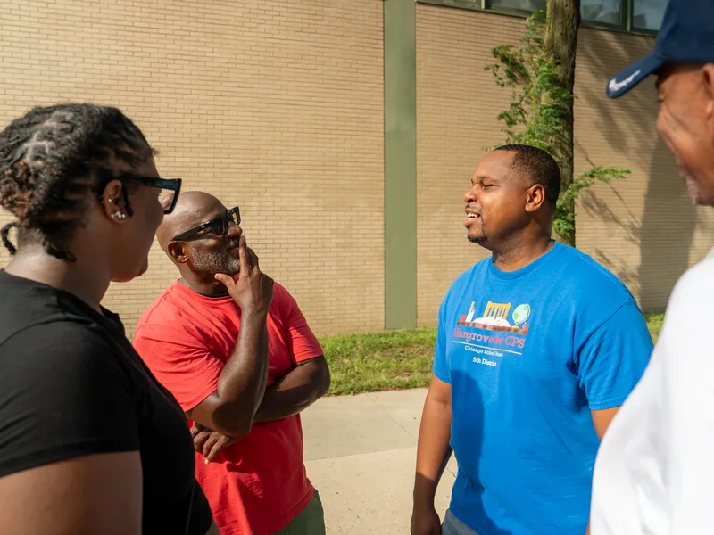 Anthony Hargrove talking with adults beside trees outdoors.