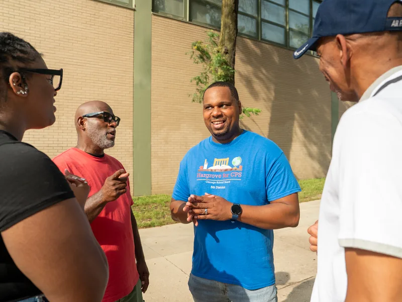 Anthony Hargrove with his hands clasped, listening to adults outdoors.