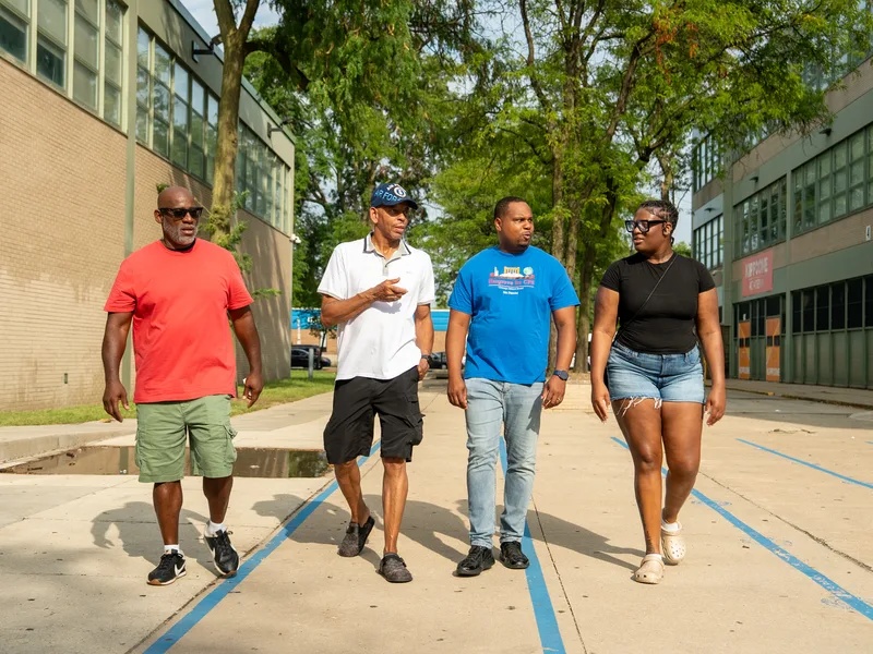 Anthony Hargrove walking with adults along a sidewalk beside a school.
