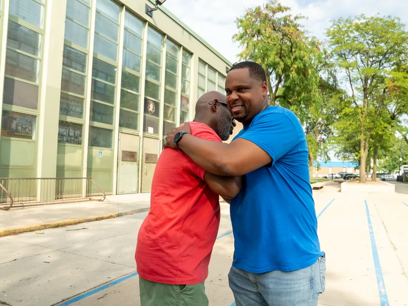 Anthony Hargrove embracing a man in a red shirt outdoors.