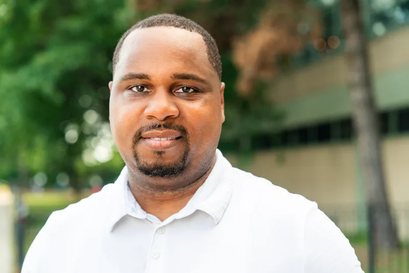 Anthony Hargrove smiling in a white polo shirt with green trees behind him.