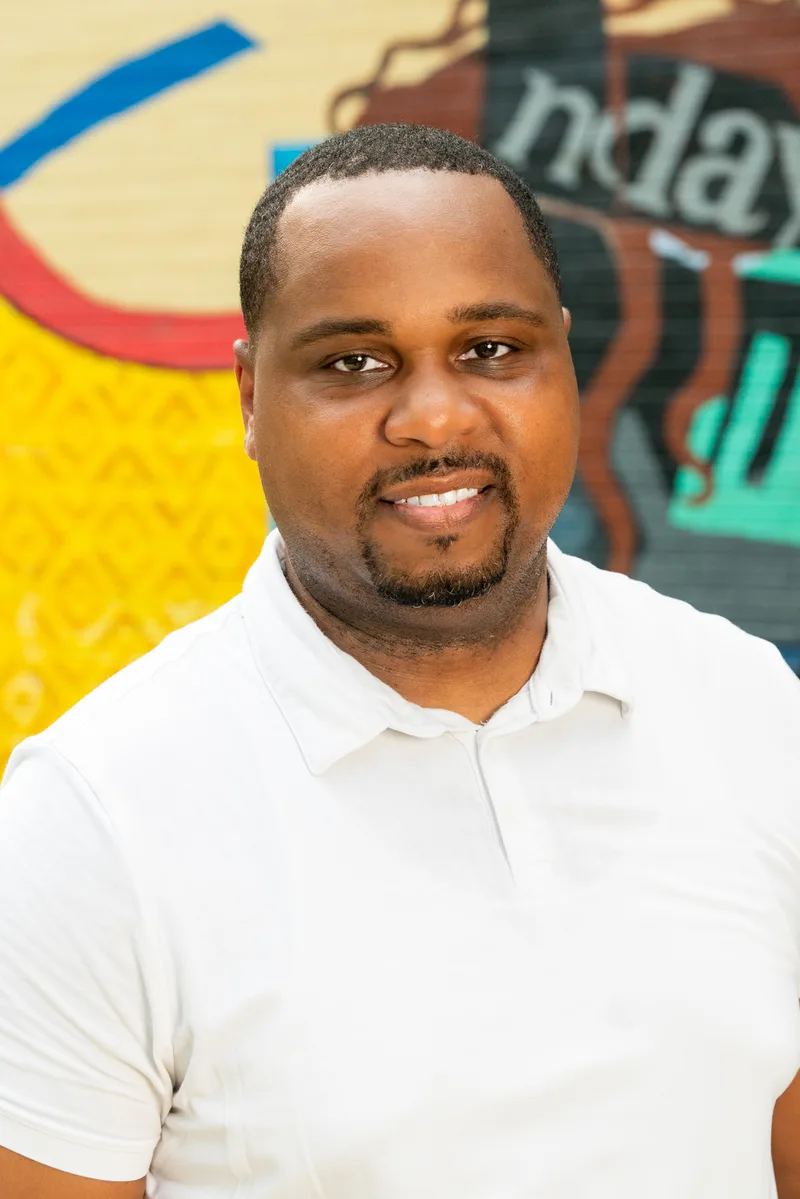 Close vertical portrait of Anthony Hargrove in a white polo shirt beside a mural.