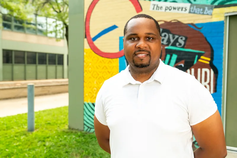 Anthony Hargrove in a white polo shirt with his hands behind his back in front of a mural.