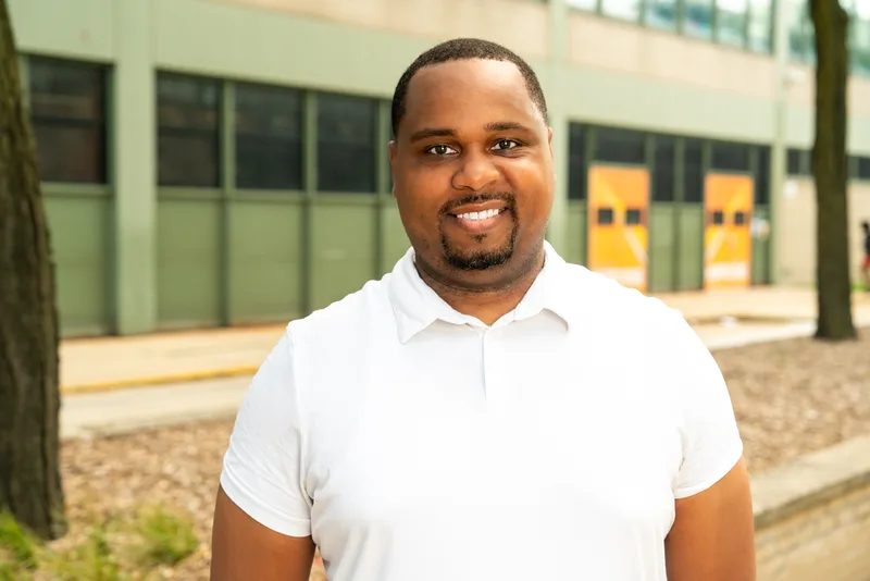 Anthony Hargrove smiling in a white polo shirt outside a school with trees nearby.